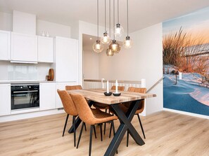 Una cocina moderna con armarios blancos, una mesa de comedor de madera con sillas, y luces colgantes.