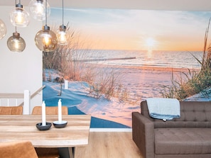 Una habitación con un amplio mural en la pared que muestra una playa al atardecer, una mesa de comedor con sillas y un sofá.