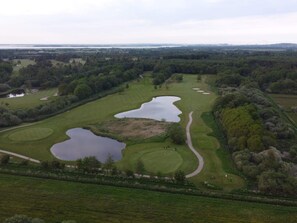 Une vue aérienne d’un terrain de golf avec plusieurs étangs, entouré d’une forêt dense et de vastes zones herbeuses.