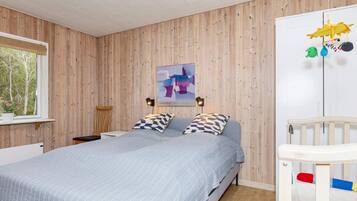 A bedroom with a bed, a crib, a window with a view, and a wall-mounted artwork.