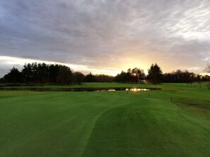 Un parcours de golf avec un étang, des arbres et un ciel nuageux.
