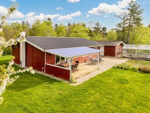 A red wooden building with a covered patio area and a greenhouse. - 6 Person Holiday Home in Nibe (Nibe)