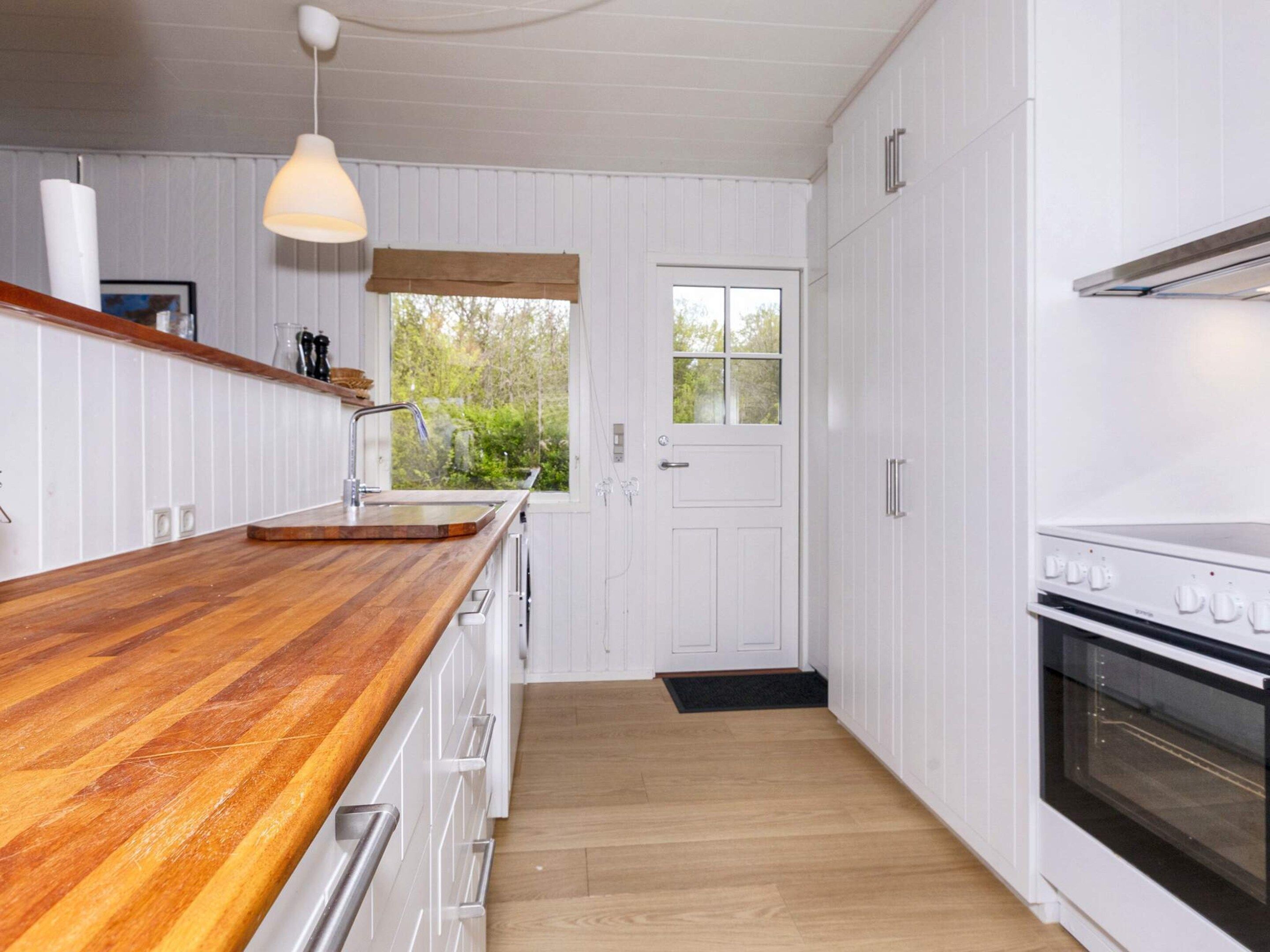 A kitchen with a wooden countertop, white cabinets, a window with a view, and a stove.