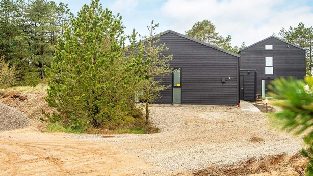 A modern building with a gravel driveway, surrounded by trees.
