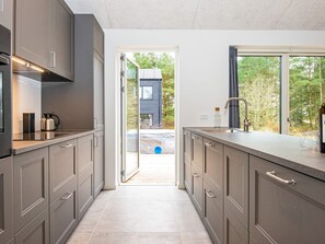 A modern kitchen with grey cabinets, a stainless steel countertop, and a view of a house through an open door.