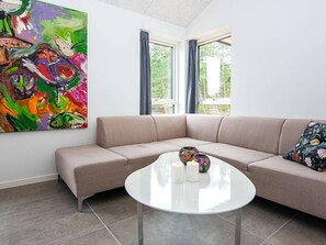 Een moderne woonkamer met een beige modulaire bank, een witte salontafel met kaarsen, en een kleurrijk abstract schilderij aan de muur.