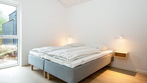 A modern bedroom with a bed, bedside lamps, and a view of the outdoors.