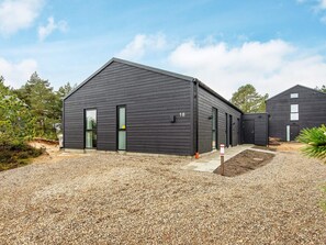 A modern building with a dark exterior, numbered 18, featuring a gravel driveway and a small garden area.