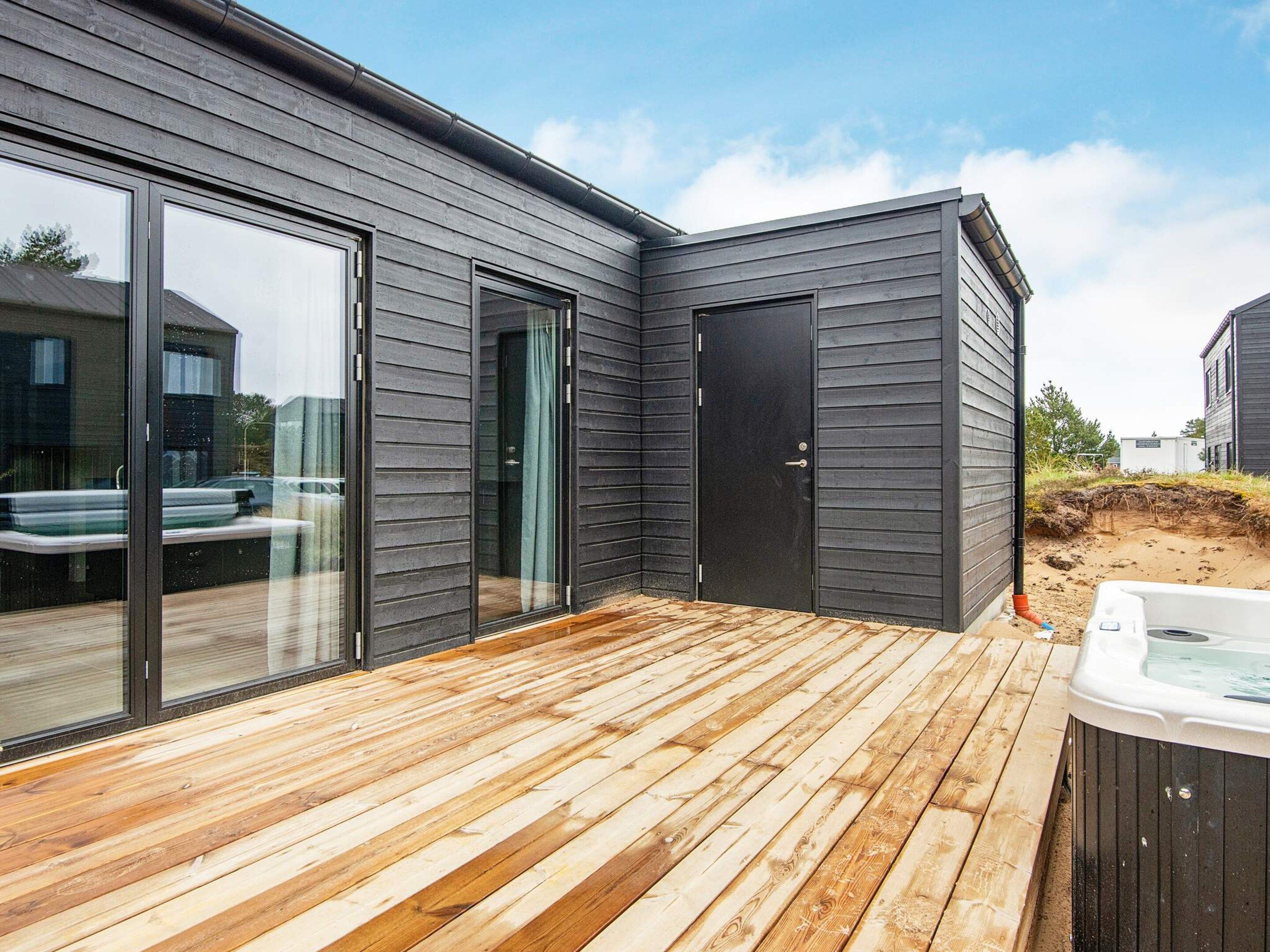 A modern house with a deck, sliding glass doors, and a hot tub.