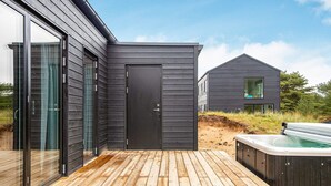 A modern outdoor deck with a wooden floor, a black door, and a hot tub.