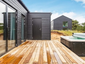 A modern outdoor deck with a wooden floor, a black door, and a hot tub.
