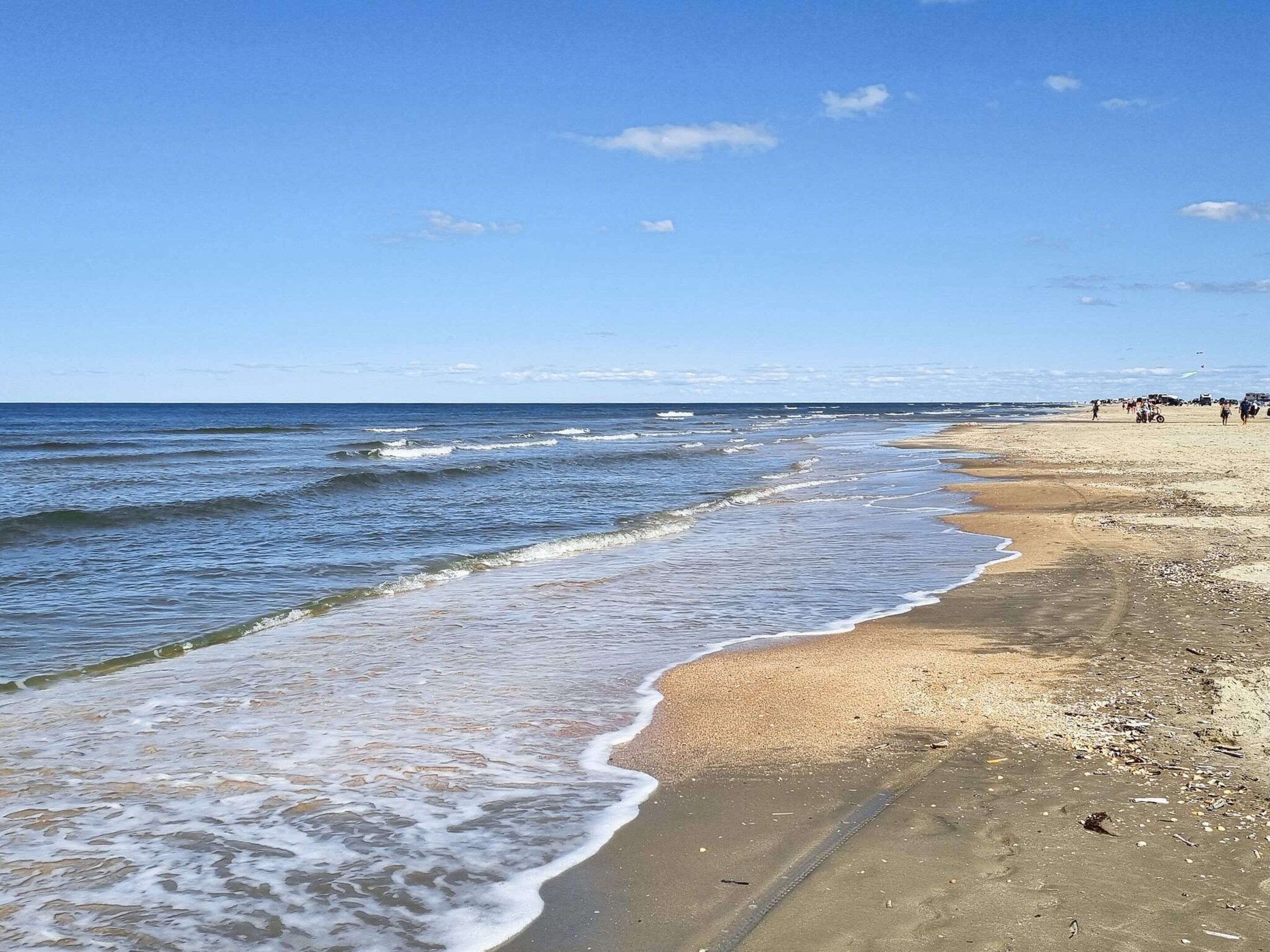 Une plage avec des vagues, un ciel dégagé et des gens qui se promènent.
