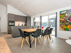 Een moderne keuken met grijze kastjes, een houten eettafel met zwarte stoelen, en een groot raam.