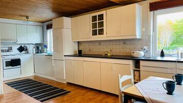 A kitchen with wooden cabinets, a stove, and a window with a view of trees.