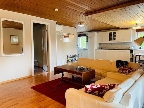 A living room with a sofa, a coffee table, and a red rug. There is a kitchen area with cabinets and a window.