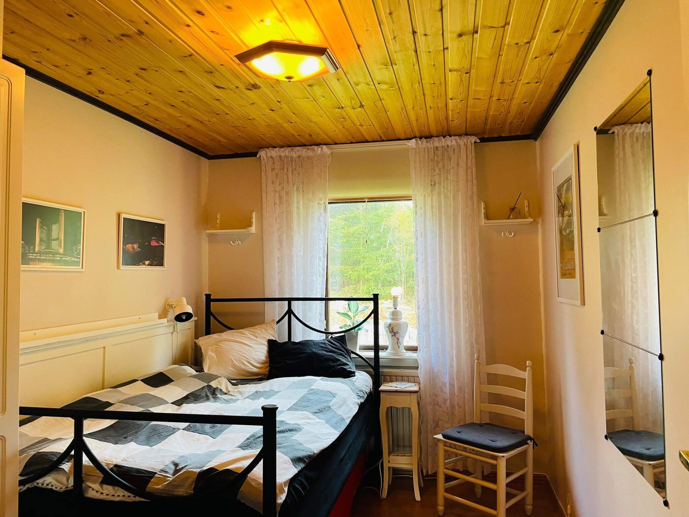 Ett sovrum med en säng, en stol, ett litet bord och ett fönster med gardiner.