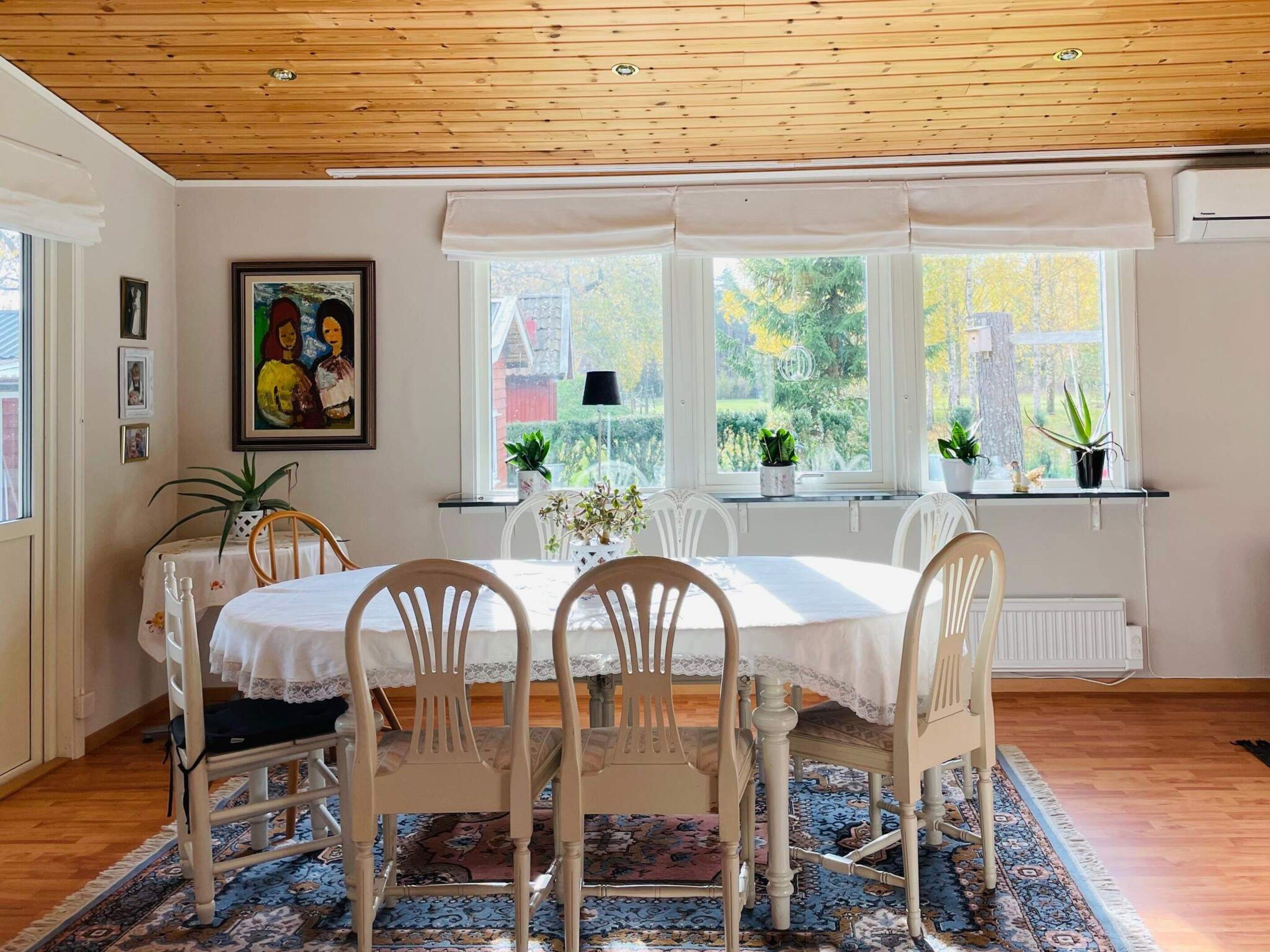 A dining area with a table and chairs, a window with a view of greenery, and a ceiling with wooden beams.