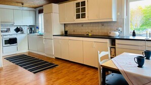 Une cuisine avec des meubles de rangement en bois, une cuisinière, un réfrigérateur et une fenêtre donnant sur les arbres.