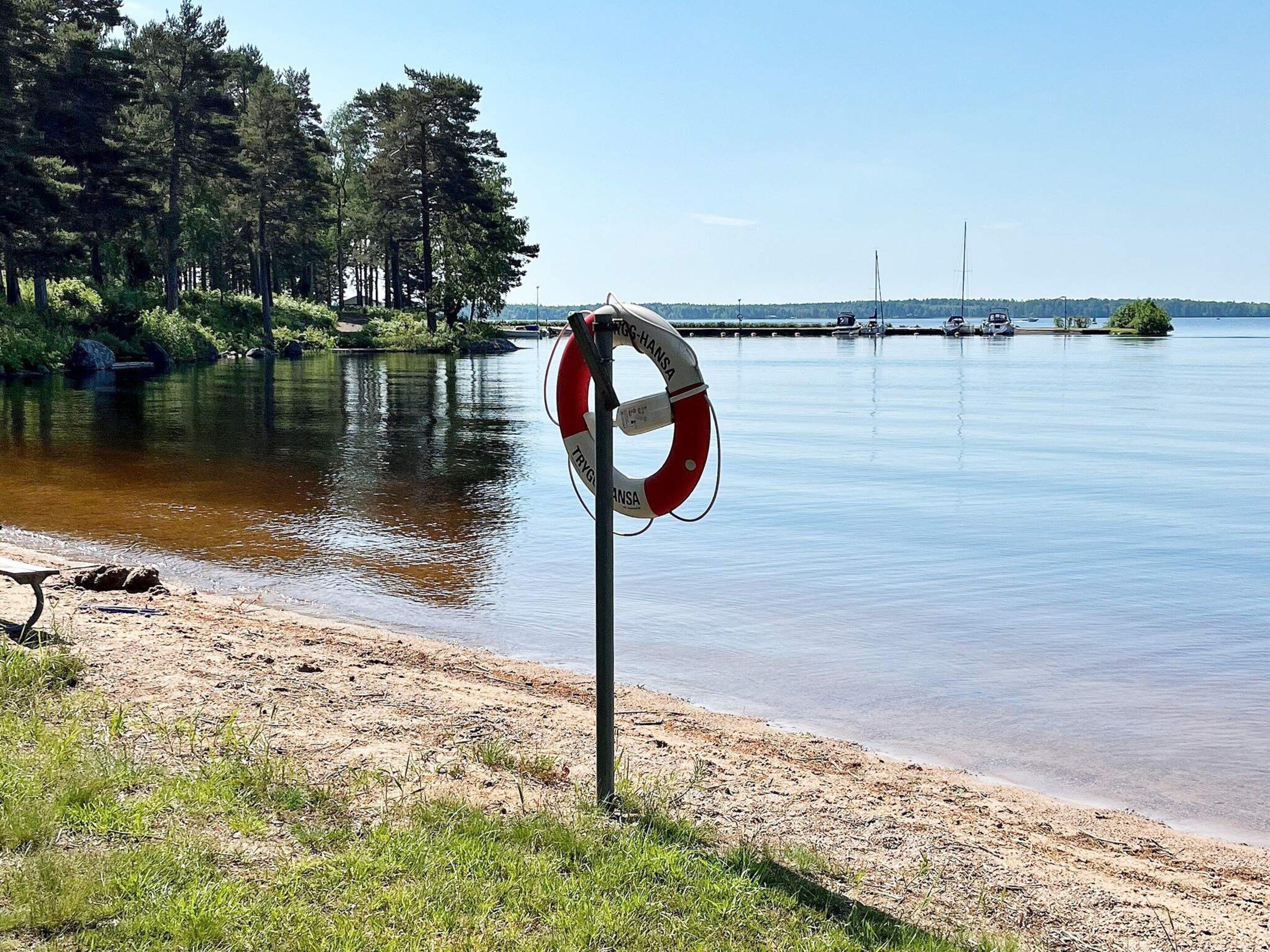 A lifebuoy on a sandy beach with calm water and trees in the background.