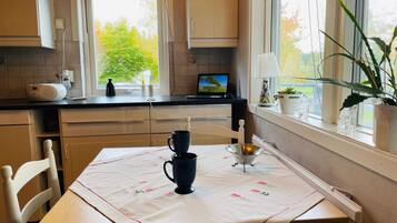 Una cocina con una mesa de comedor, sillas, un ventanal con vistas a árboles y una planta en maceta en el alféizar.