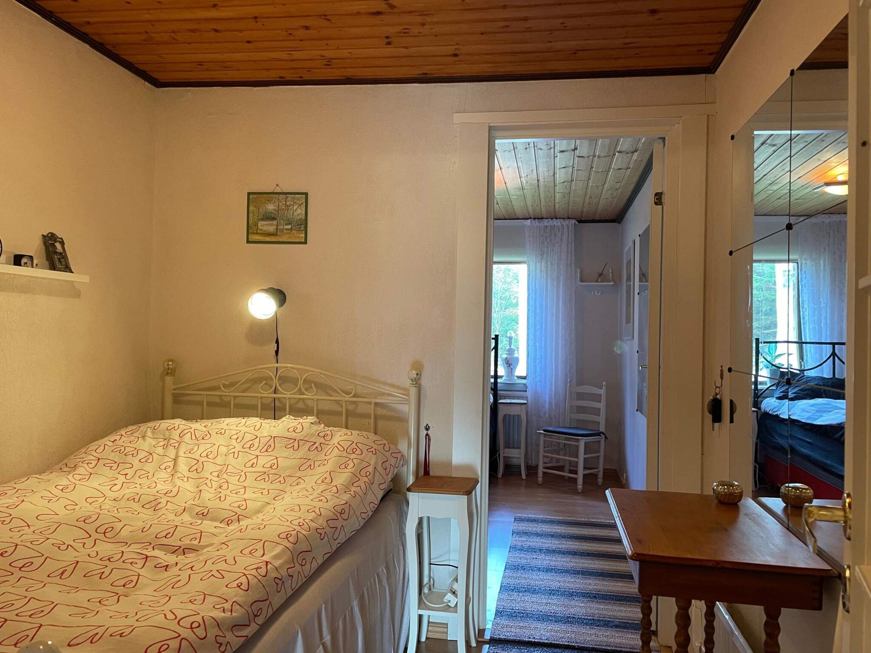 Un dormitorio con cama, lámpara de noche y vista hacia otra habitación.