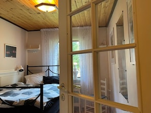 A room with a bed, a window with curtains, a door with glass panels, and a ceiling light fixture.