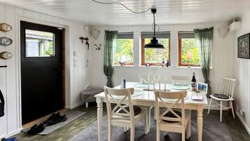 A dining area with a white table, four chairs, a black pendant light, and a window with curtains.