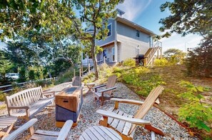 Una casa con cimientos de piedra, una terraza de madera y asientos exteriores, incluyendo sillas y un banco.