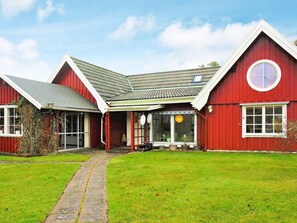 Un bâtiment de couleur rouge, de style grange, avec un toit en pente, un porche à l’avant et une fenêtre circulaire sur le côté droit.