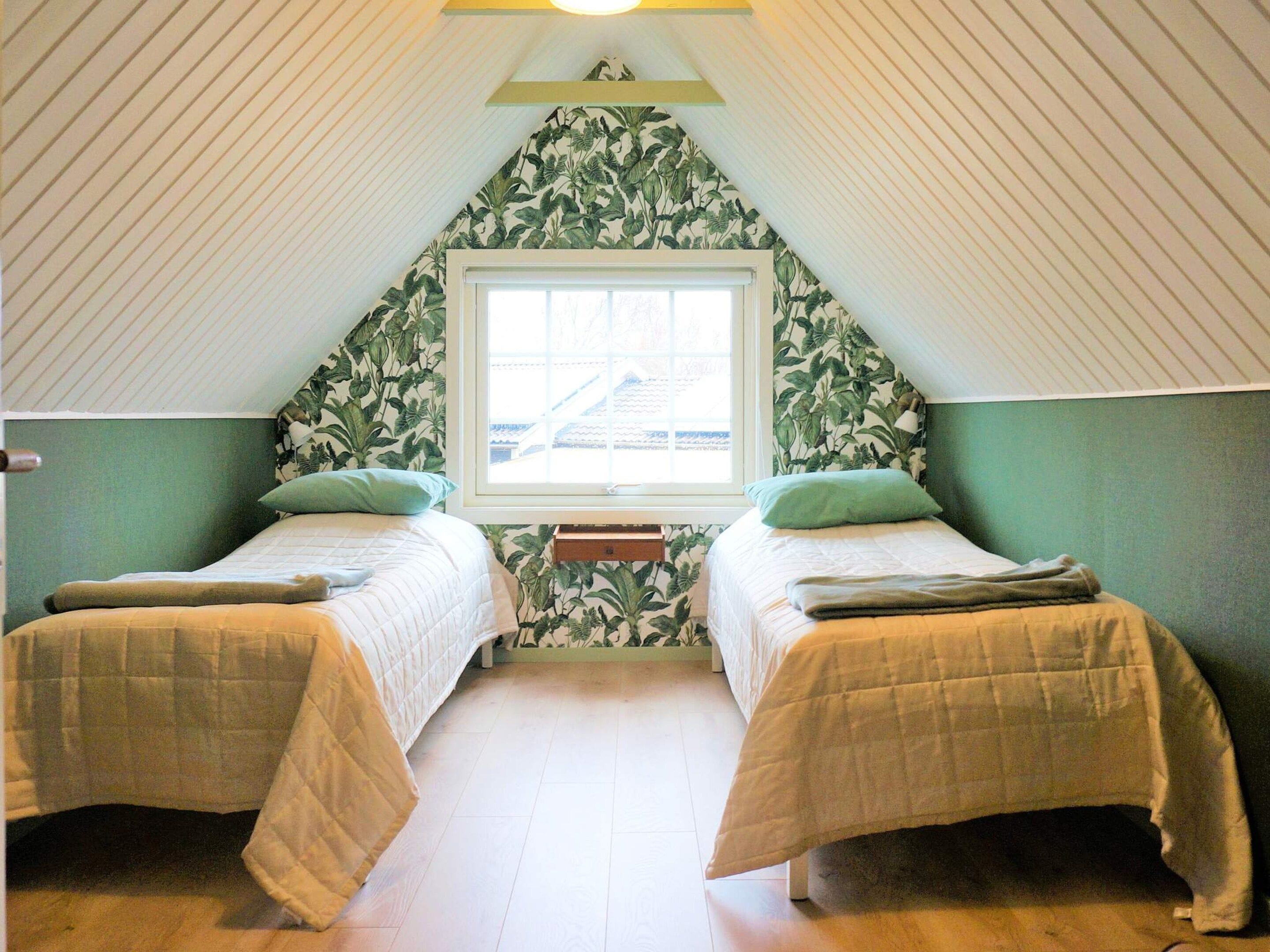 Une chambre avec deux lits, une fenêtre et un plafond en pente.