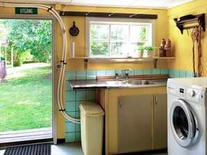 Une cuisine compacte équipée d’un lave-linge, d’un évier et d’une fenêtre donnant sur un jardin.