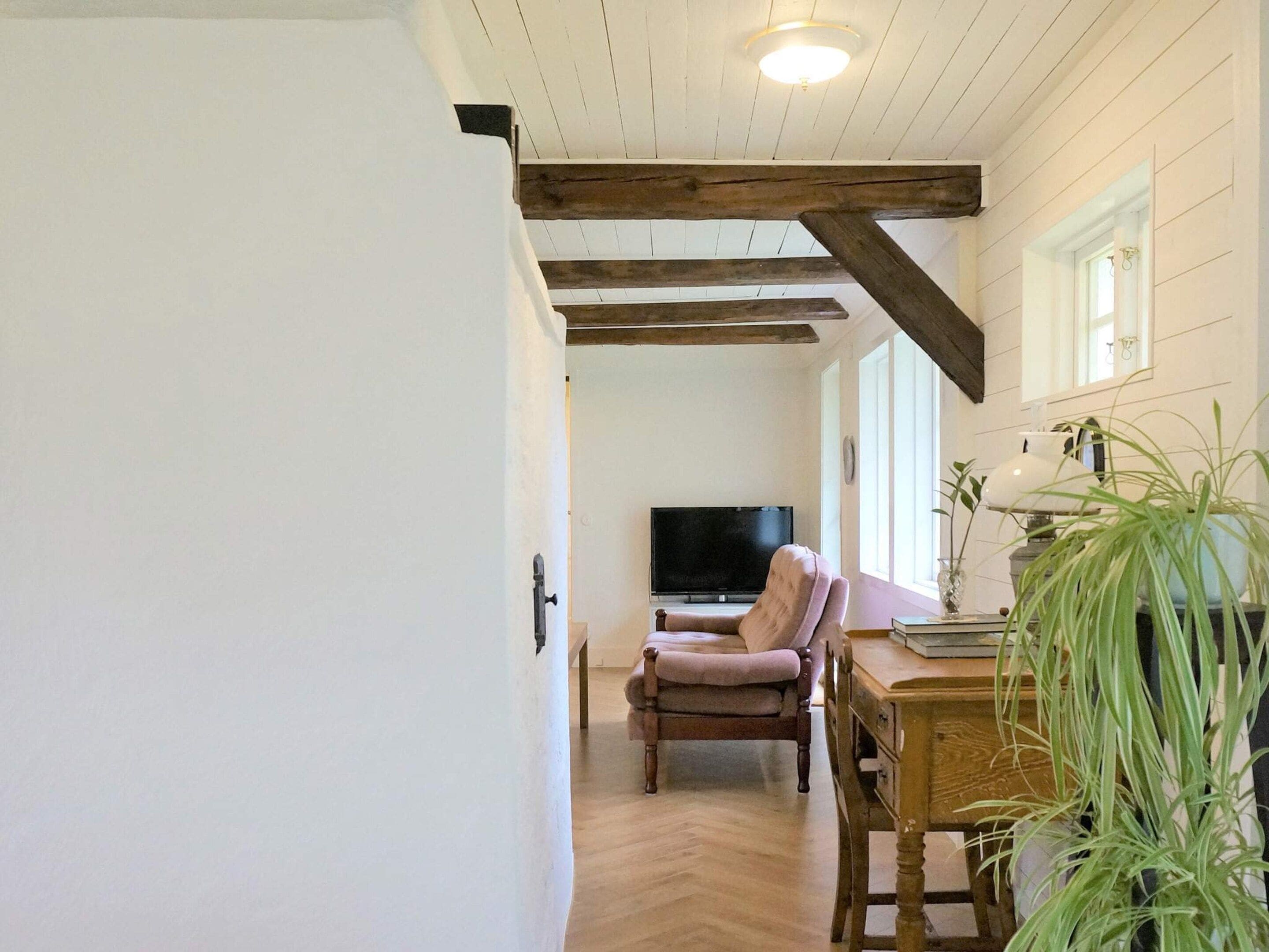 A room with a wooden ceiling, a television, a chair, a table, and a potted plant.