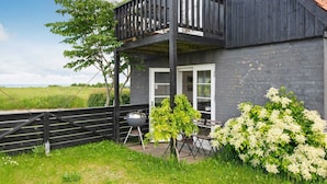 A two-story house with a balcony, a barbecue grill, and a garden with white flowers. - 5 Person Holiday Home in Knebel (Knebel)