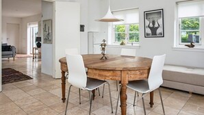 A spacious dining area with a wooden table and white chairs, a pendant light, and a view of greenery outside through large windows. - 5 Person Holiday Home in Knebel (Knebel)