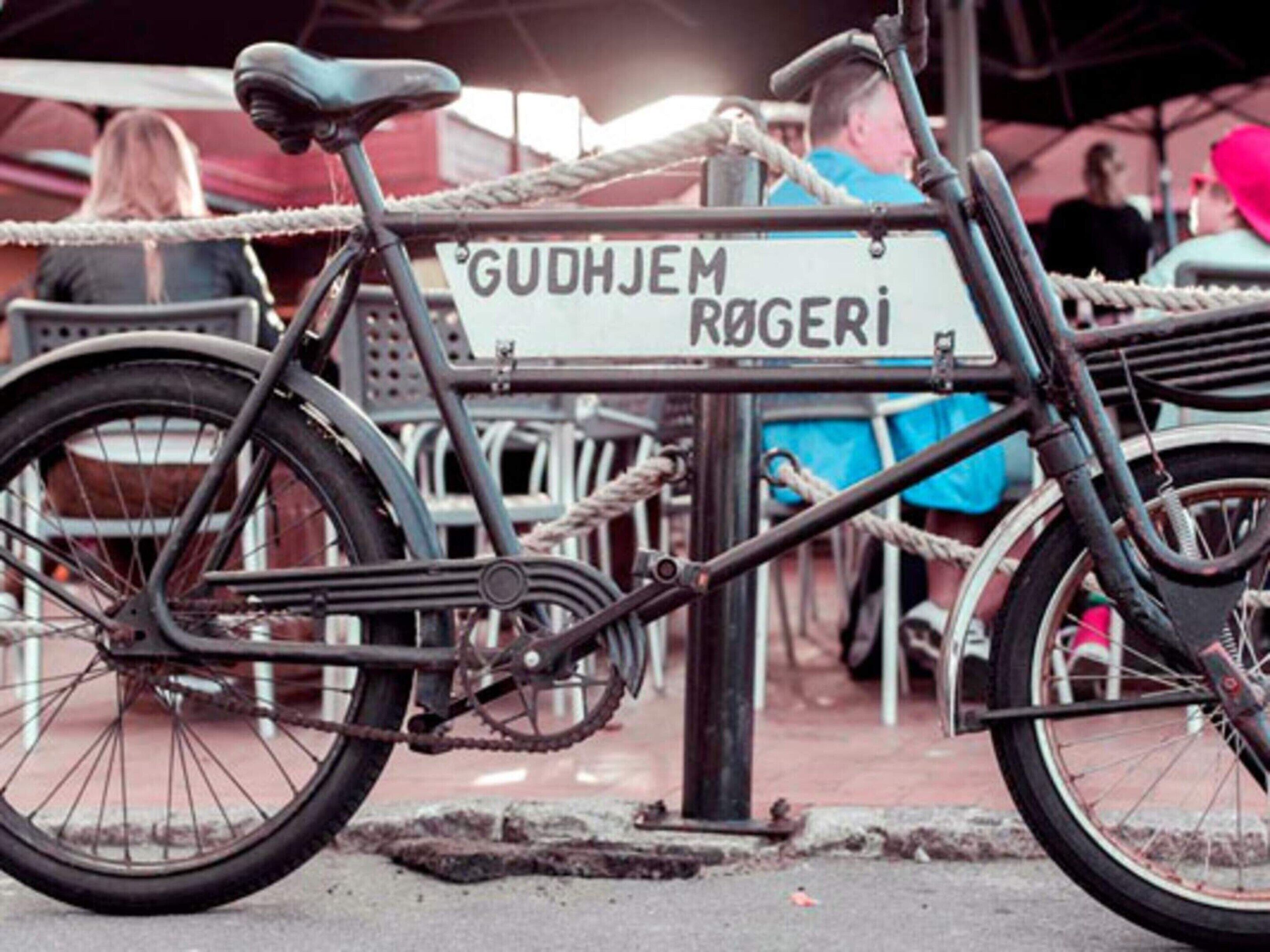 A bicycle parked next to a sign that reads "GUDHJEM ROGERI".