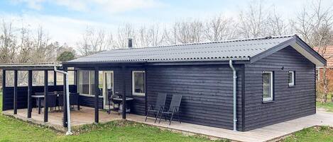 Eine kleine, dunkle Holzhütte mit einer überdachten Terrasse und einem Grill.