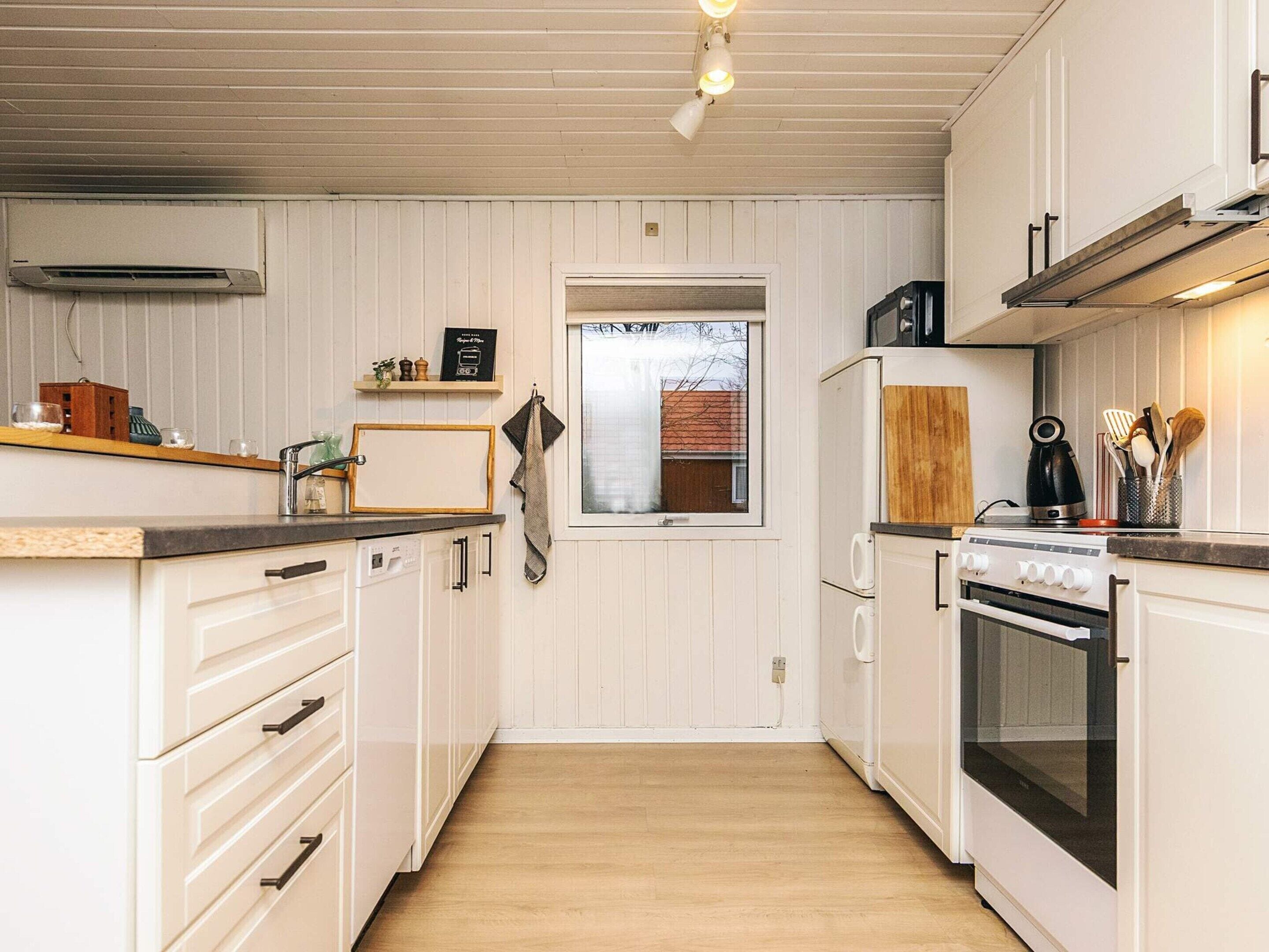 A kitchen with white cabinets, a wooden countertop, a window, and a stove.