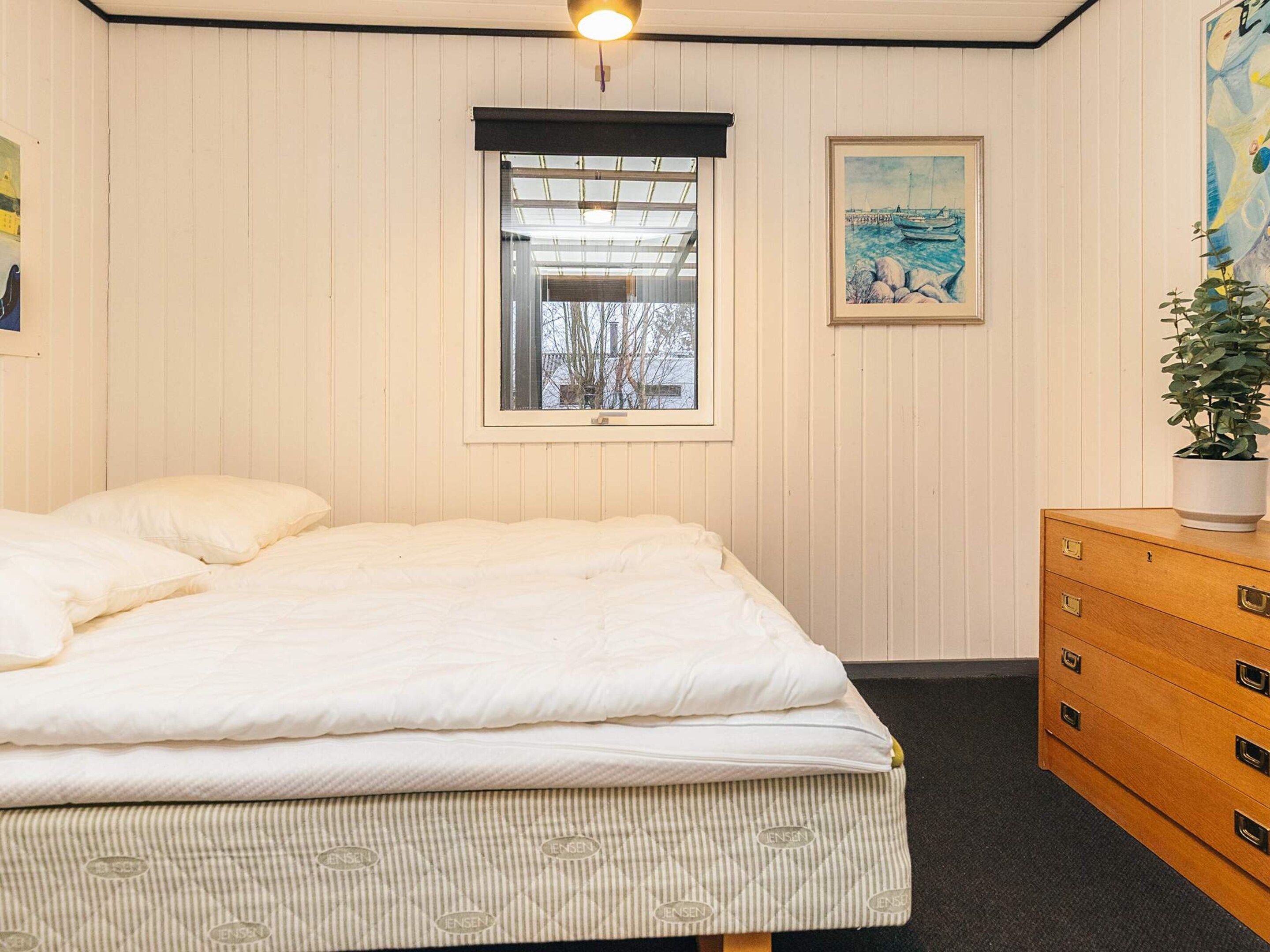 A bedroom with a bed, a window, a dresser, and a painting on the wall.