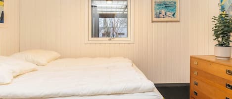 A bedroom with a bed, a window, a dresser, and a painting on the wall.