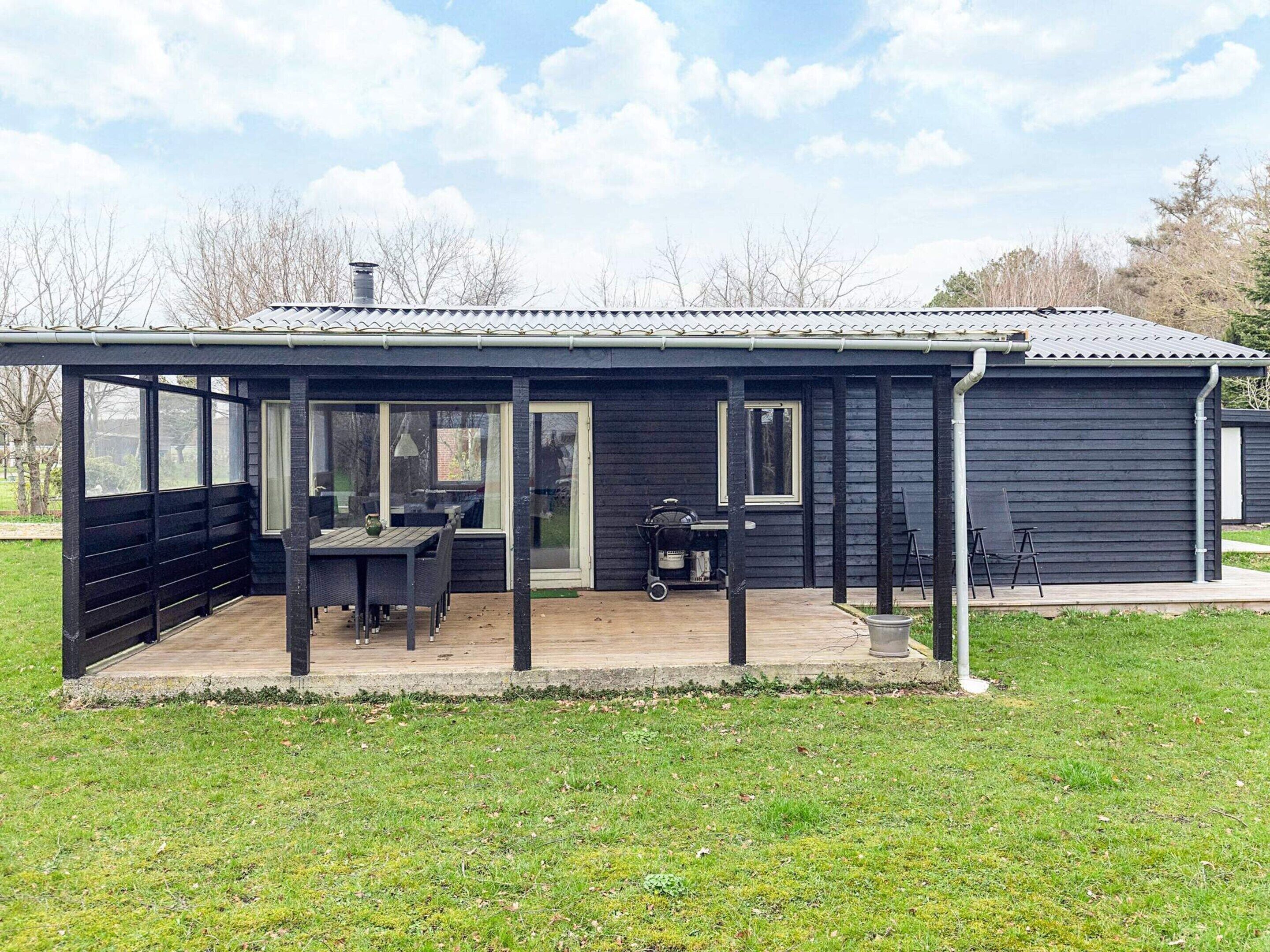 A black building with a covered patio, a table, chairs, and a grill.