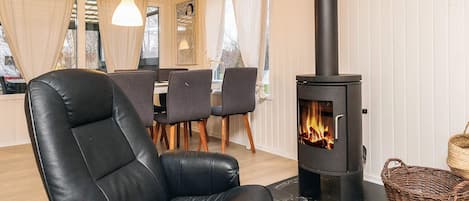 A cozy room with a black leather chair, a table with chairs, a woven basket, and a wood-burning stove.