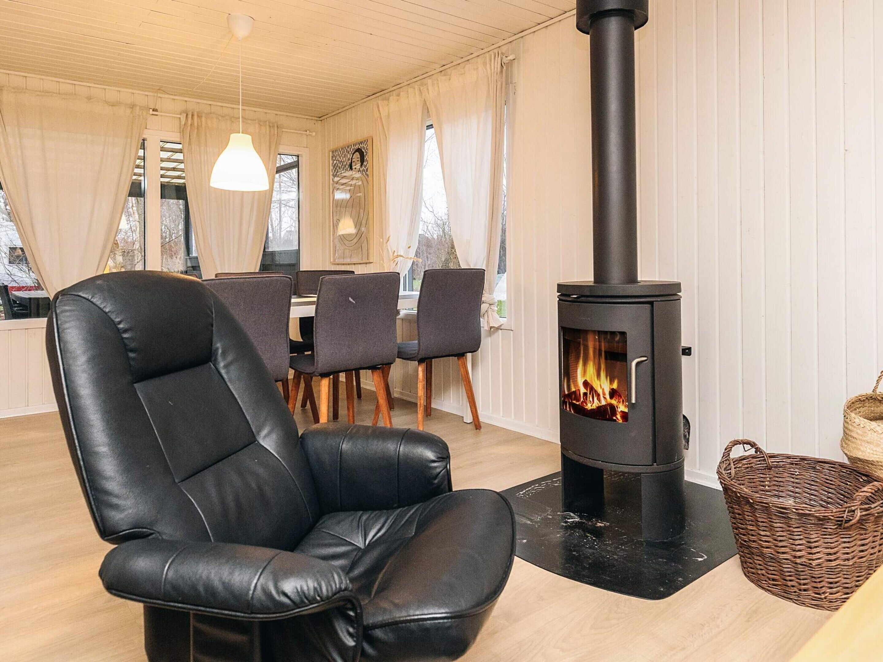 A cozy room with a black leather chair, a table with chairs, and a wood-burning stove.