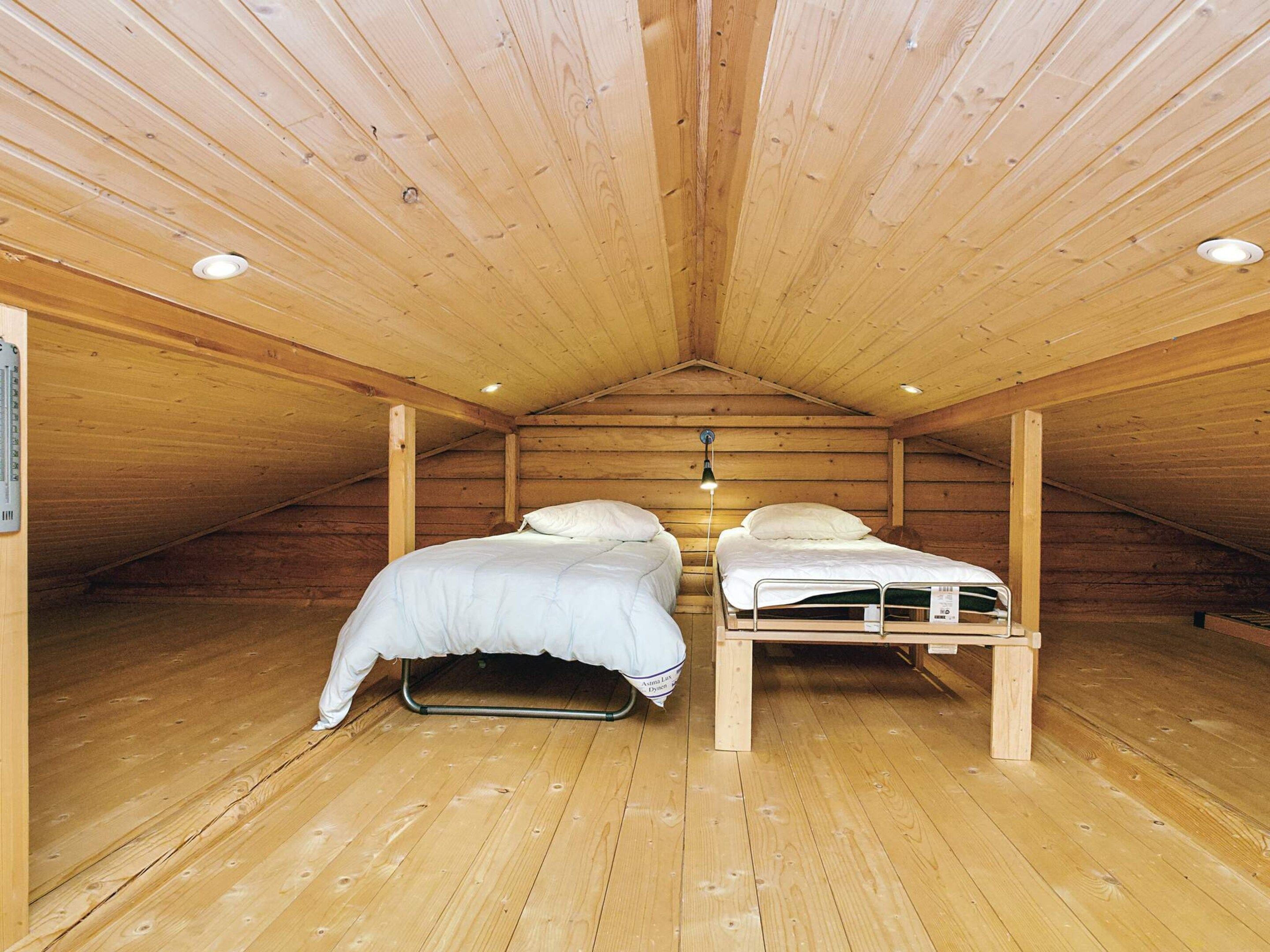 A small attic bedroom with two beds, wooden walls, and a sloped ceiling.