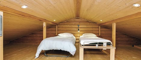 A small attic bedroom with two beds, wooden walls, and a sloped ceiling.