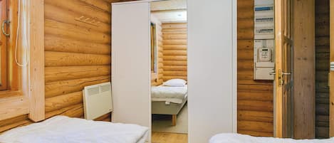 Une chambre dans un chalet en bois, avec deux lits, une armoire blanche et un tableau électrique visible.