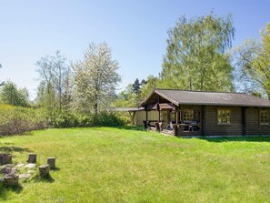 A log cabin with a porch, surrounded by a grassy field and trees. - 6 Person Holiday Home in Eskebjerg (Eskebjerg)