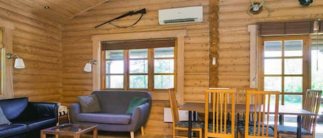 Et interiør af en træhytte med sofa, spisebord, stole og pejs.
