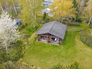 En hytte med veranda, omgivet af træer og en græsplæde.