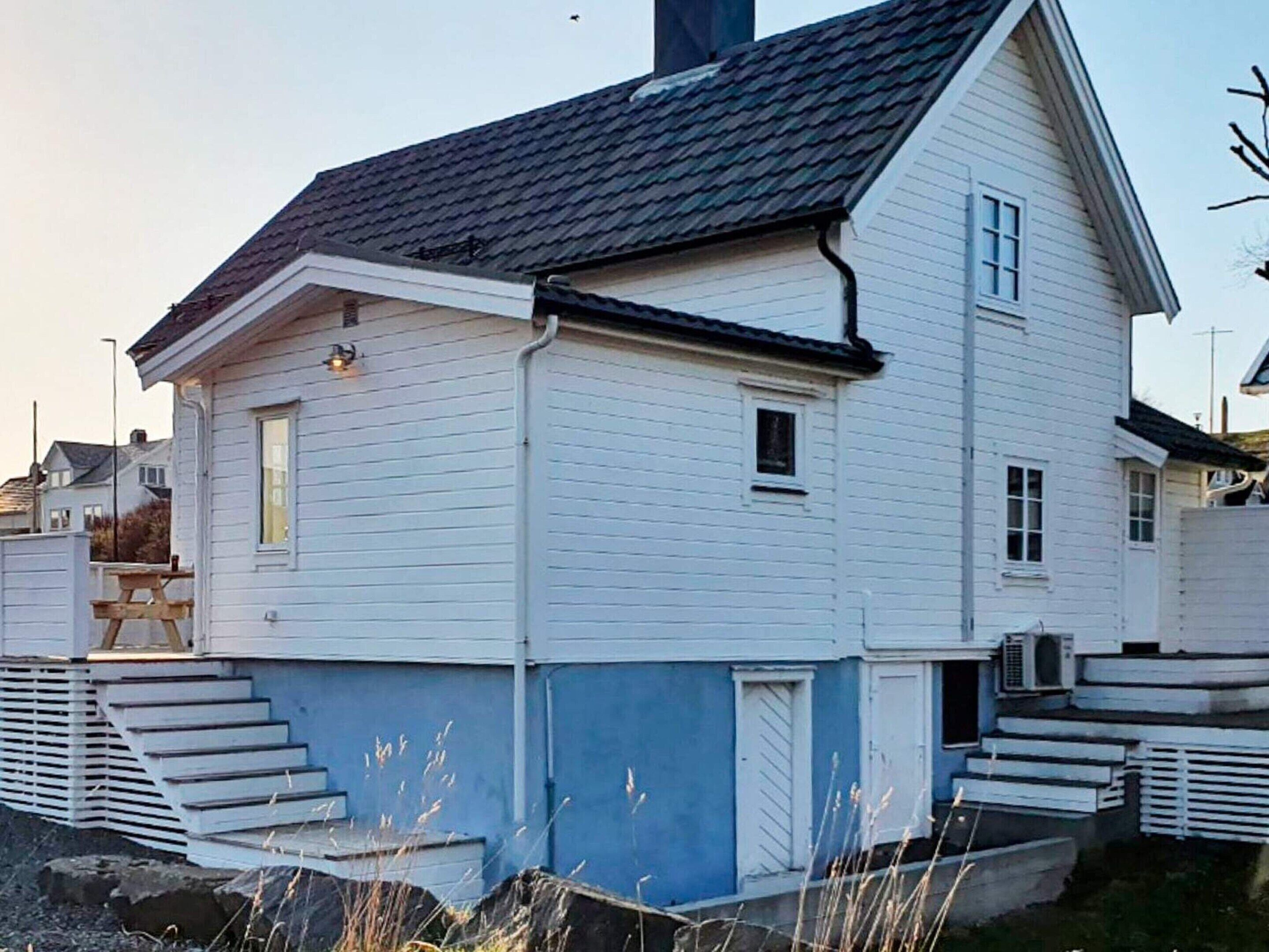 Une maison à deux étages, dotée d’un toit à forte pente, d’un porche à l’avant avec des marches et d’une petite fenêtre au deuxième étage.