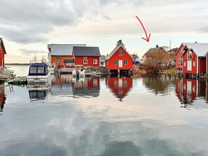 Une scène de bord de mer avec des bâtiments rouges, des bateaux et une eau calme qui reflète les constructions.